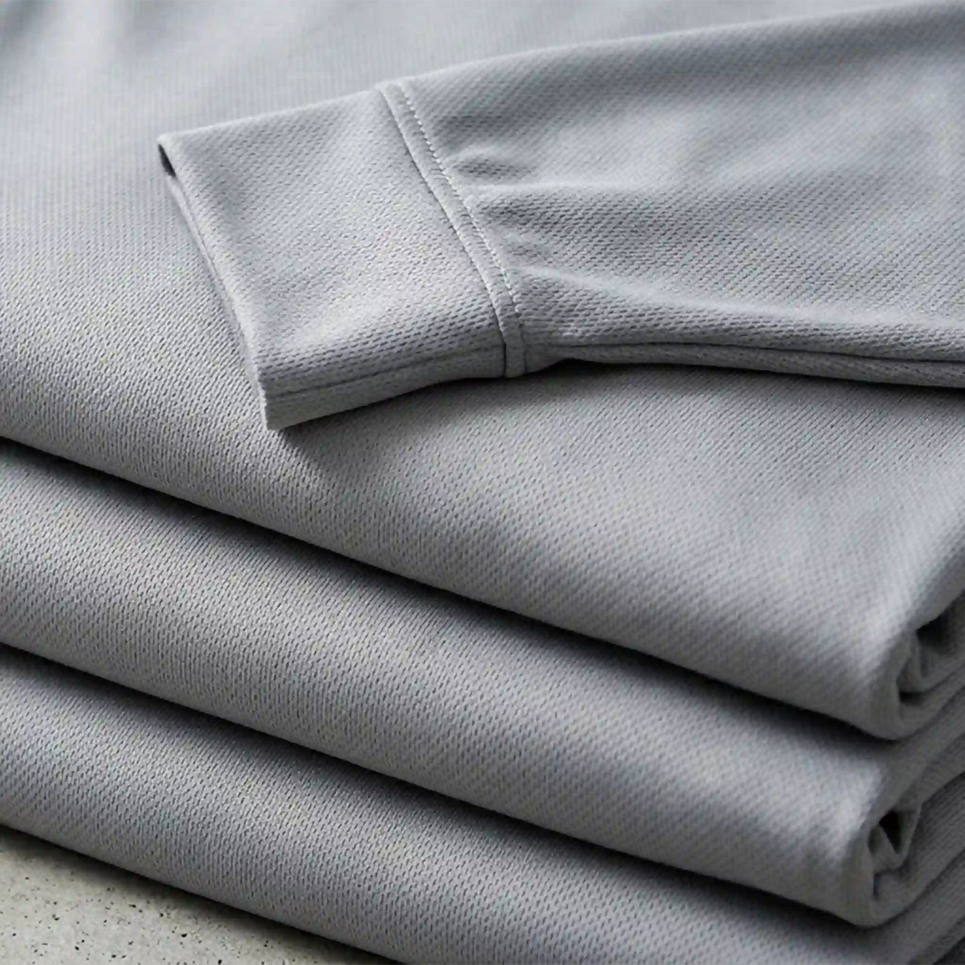 A stack of folded long-sleeve performance shirts showing high-quality fabric texture and durable collar construction - Made in Mount Pearl, NL.