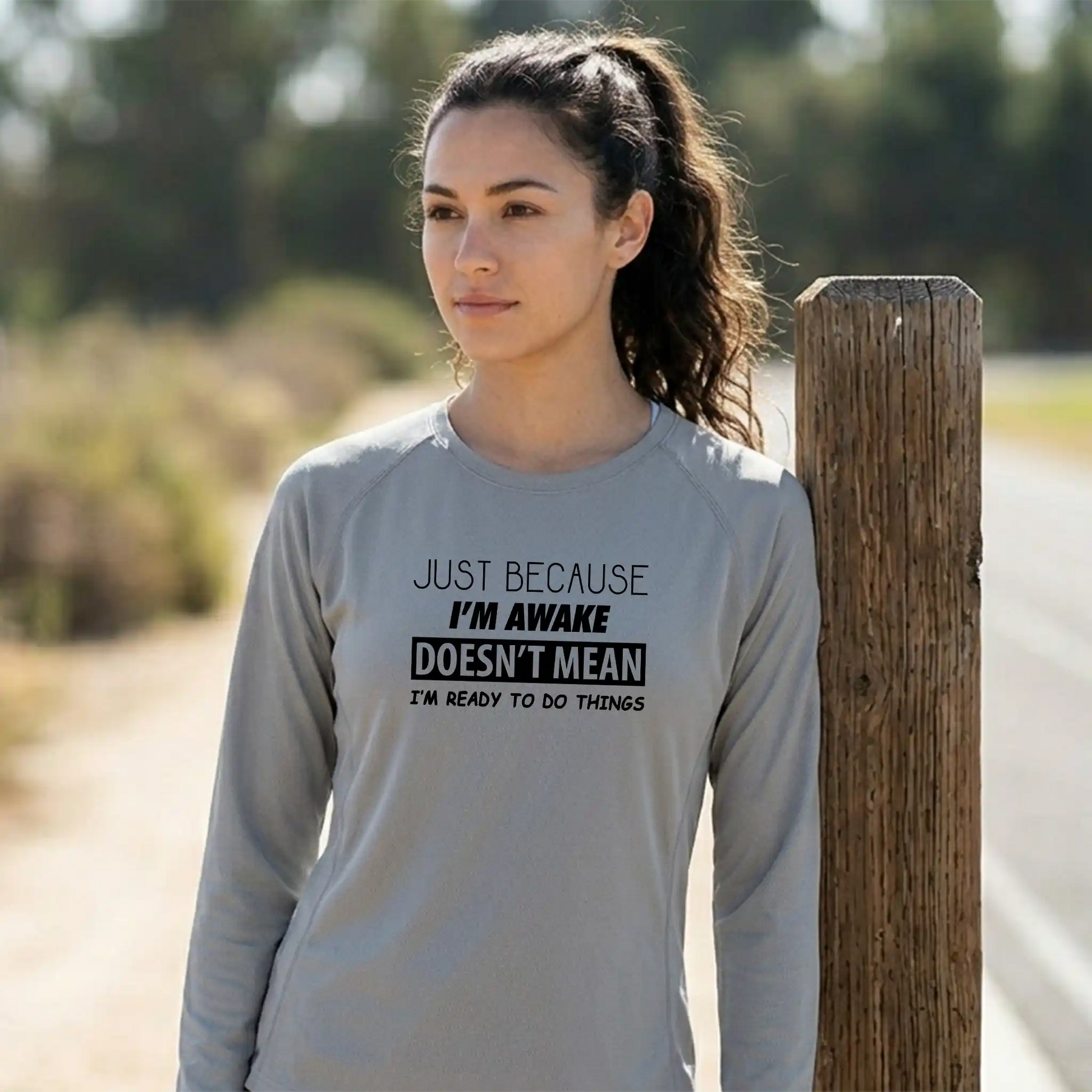 Female model in a long-sleeve Platinum moisture-wicking shirt featuring 'Just Because I'm Awake' slogan - Comfortable weekend gear.