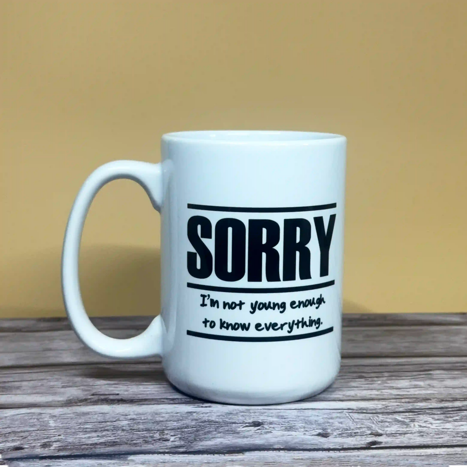 15oz white ceramic coffee mug with black text reading "Sorry, I'm not young enough to know everything" in a clean modern font