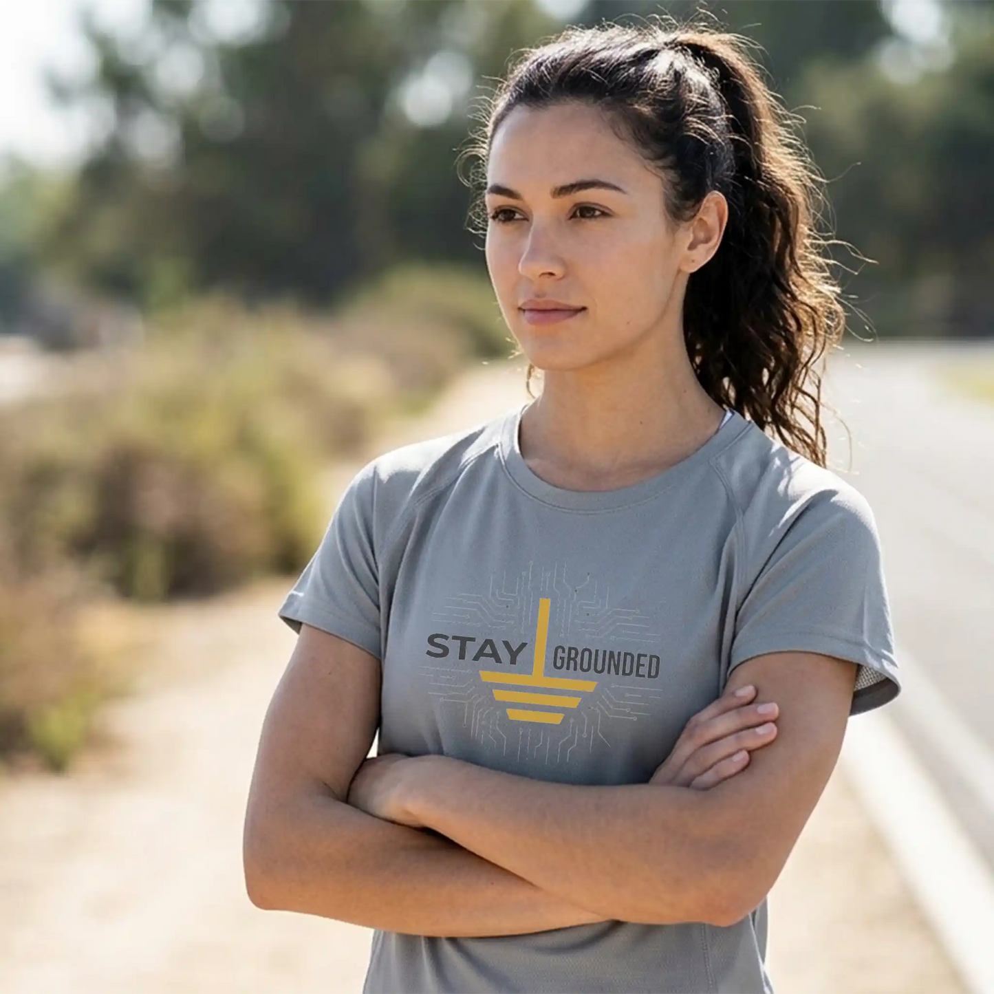 Female athlete wearing a short-sleeve Core365 CE10 Platinum performance tee with the 'Stay Grounded' design, standing on an outdoor running trail.